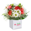 Spring gathered in a moment-this joyful bouquet shines from within a spotless white gift bag, ready to bring delight to someone in Motspur Park. Fluffy coral and peach carnations unfurl their ruffled petals, radiating warmth and gentle fragrance, while clusters of cheerful white daisies with luminous yellow-green centers add a touch of sunshine. Wisps of white baby's breath drift playfully throughout, their cloud-like blooms evoking local morning mists over Cannon Hill Common. Soft, glossy deep green leaves embrace the bouquet, bringing structure and emphasizing its round, welcoming shape. Tucked among the blooms, hints of purple from unopened buds create quiet drama-just enough to pique curiosity and add depth. Every stem is thoughtfully placed by hand, reflecting the skilled artistry found in the neighbourhood's trusted florists. The white gift bag, ribbon-handled and pristine, whispers promise of an uplifting delivery-whether to celebrate a birthday, offer heartfelt thanks, or simply surprise a loved one living near the heart of Motspur Park. This fresh arrangement, both elegant and joyous, carries the gentle spirit of the area, capturing the simple pleasure of giving and receiving flowers.